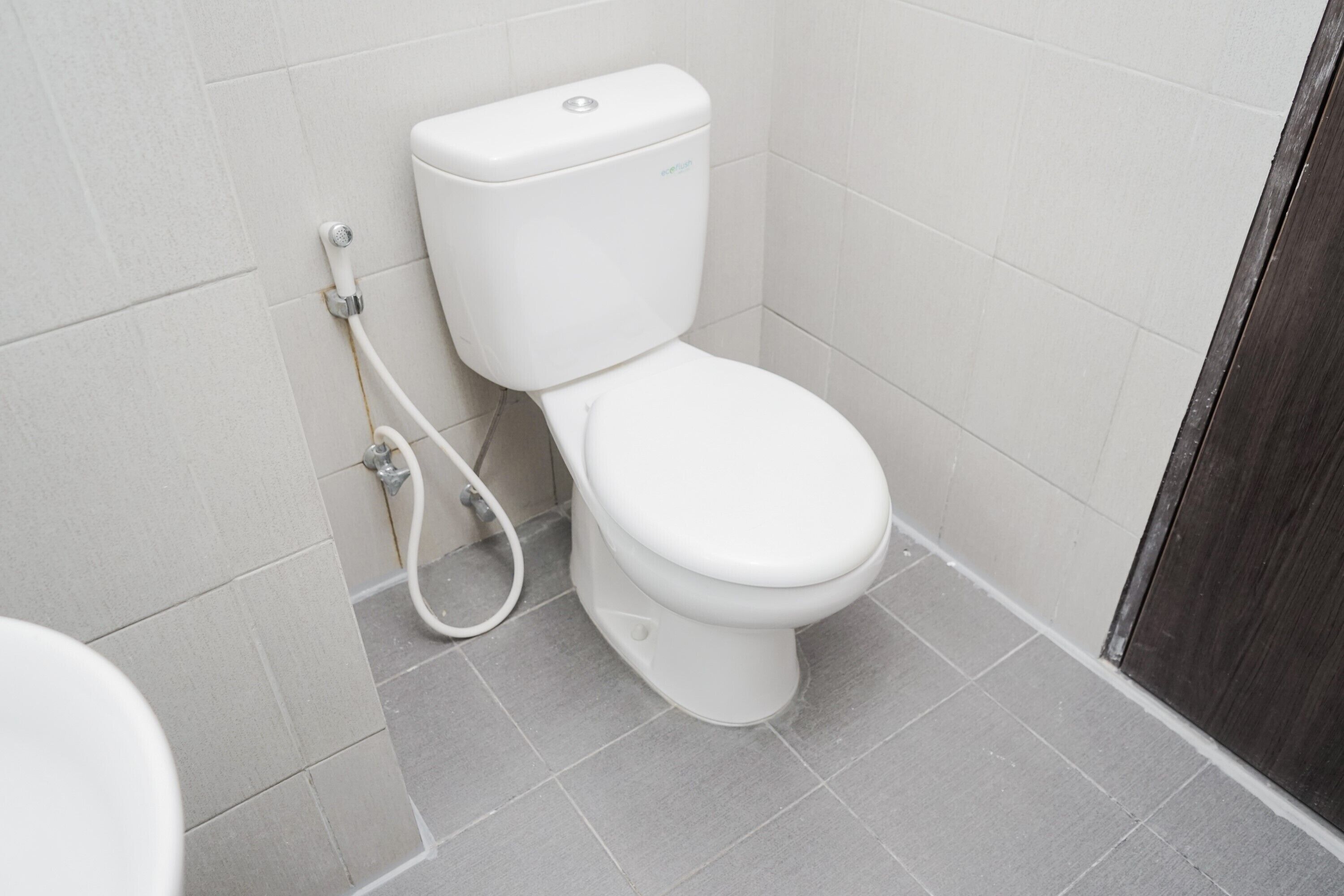 A white toilet with a tank and a seat, connected to a wall-mounted flush handle.