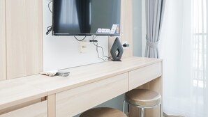 A hotel room with a wooden desk, a flat-screen TV mounted on the wall, a power strip, and two cushioned stools. - Brand New And Good Studio At Bintaro Icon Apartment (South Tangerang)