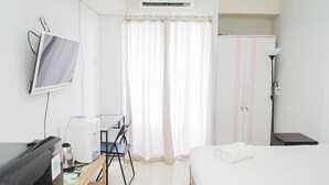 A hotel room with a bed, a desk with a chair, a television, a wardrobe, and a lamp. - Nice And Spacious Studio At Serpong Greenview Apartment (South Tangerang)