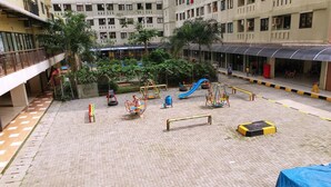 Um pátio com parquinho, incluindo balanços e escorregadores, cercado por edifícios com varandas e uma galeria coberta.