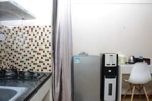 Une cuisine avec un mur recouvert de carreaux, un réfrigérateur, une machine à café et une chaise.