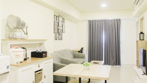 A compact living space with a kitchenette, a dining area, a grey sofa, and a TV.