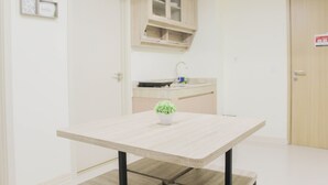 A small, clean room with a wooden table, a potted plant, and a kitchenette area.
