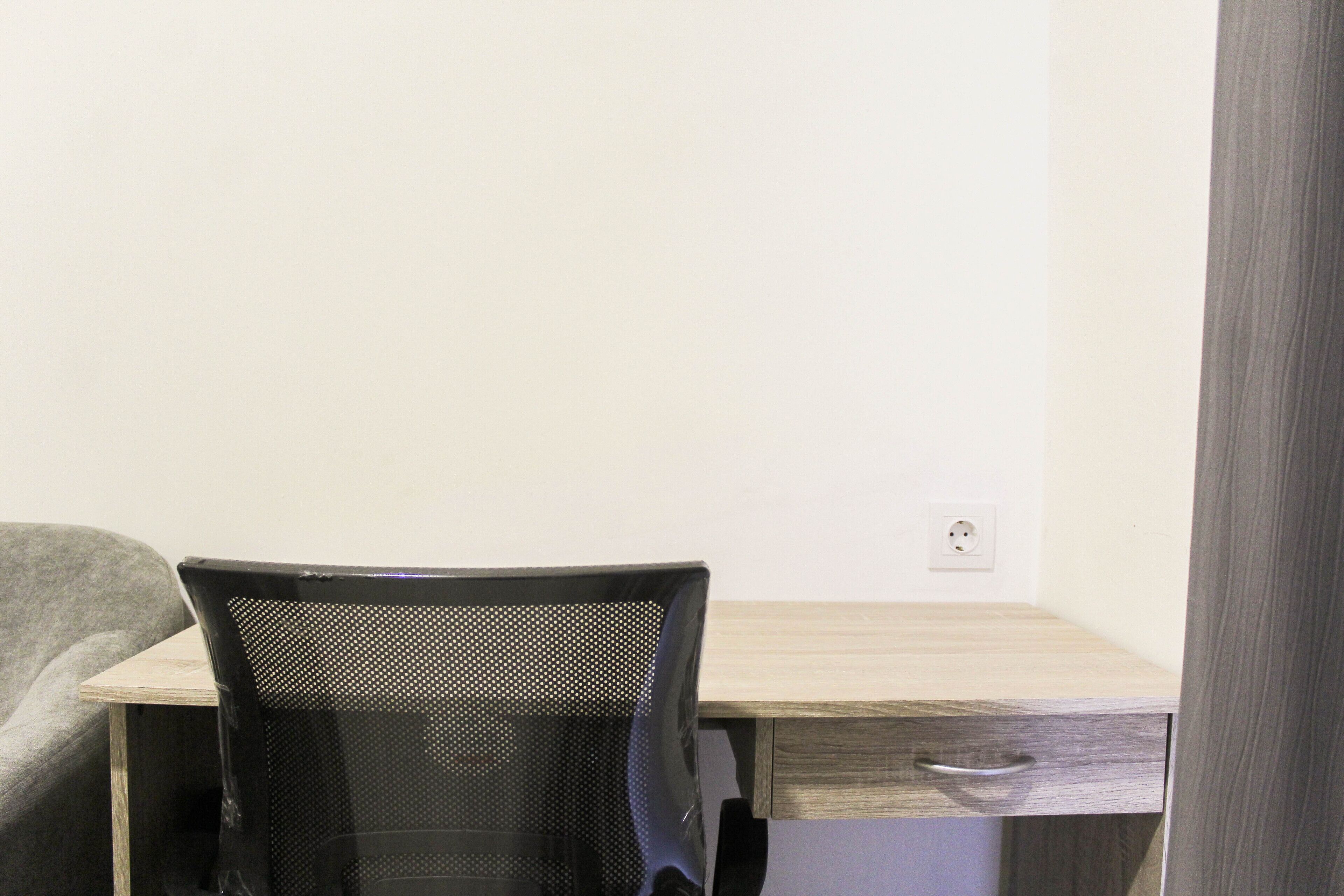 Un espacio de trabajo pequeño y moderno con un escritorio de madera, una silla de malla negra y un cajón.