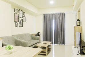 A living room with a grey sofa, a coffee table, a TV stand, and a wall with framed pictures. - Super 3Br At Meikarta Apartment (Cikarang)