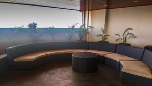Un espacio al aire libre con asientos curvos y una mesa redonda, rodeado de plantas en macetas.