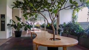 Un pasillo con plantas en macetas, un banco de madera y un cartel que indica una sala de estar.