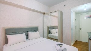 A hotel room with a bed, a mirror, a door, and a small table with a remote control and towels. - Strategic Studio At Springlake Summarecon Apartment Bekasi (Bekasi)