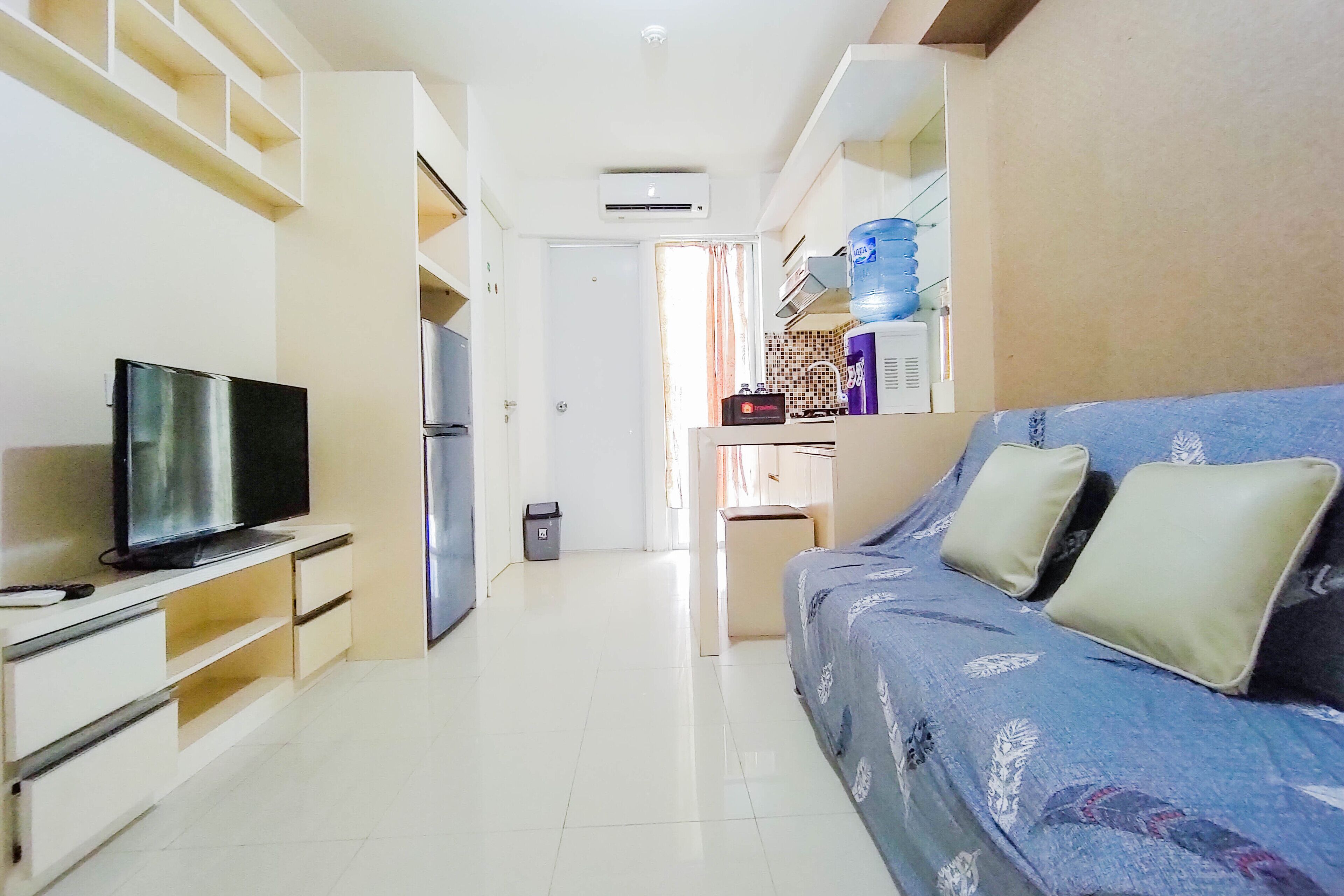 Un espacio habitable pequeño con un sofá, un televisor, una zona de cocina y un cubo de basura.