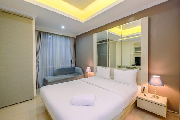 A hotel room with a large bed, a bedside table with a lamp, a wardrobe, and a window with curtains.
