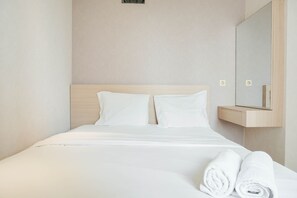 A hotel room with a bed, two pillows, a wooden headboard, a mirror, and two rolled towels.