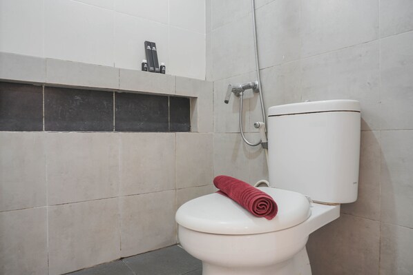 A toilet with a red towel on the seat, a showerhead, and a soap dispenser on the wall.