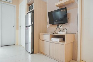 A compact kitchen with a built-in refrigerator, a microwave, and a flat-screen TV mounted on the wall.