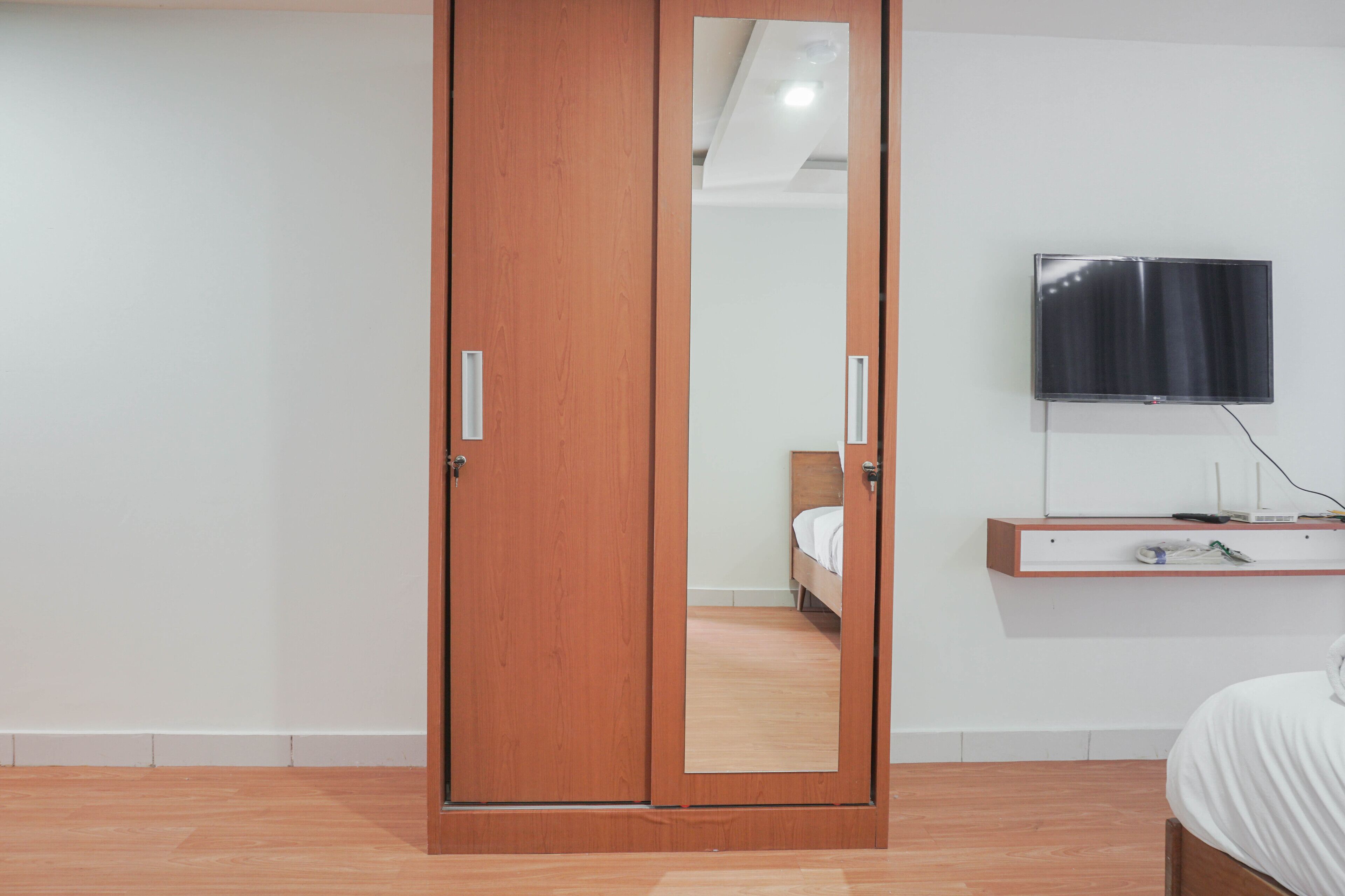 Un dormitorio con un armario de madera, una cama, una mesita de noche, un televisor montado en la pared y un espejo en la puerta del armario.