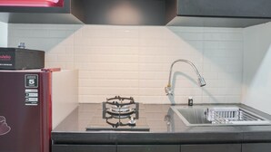 A kitchen with a gas stove, sink, and a red appliance on the left. - Scenic And Strategic Studio Amethyst Apartment (Jakarta)