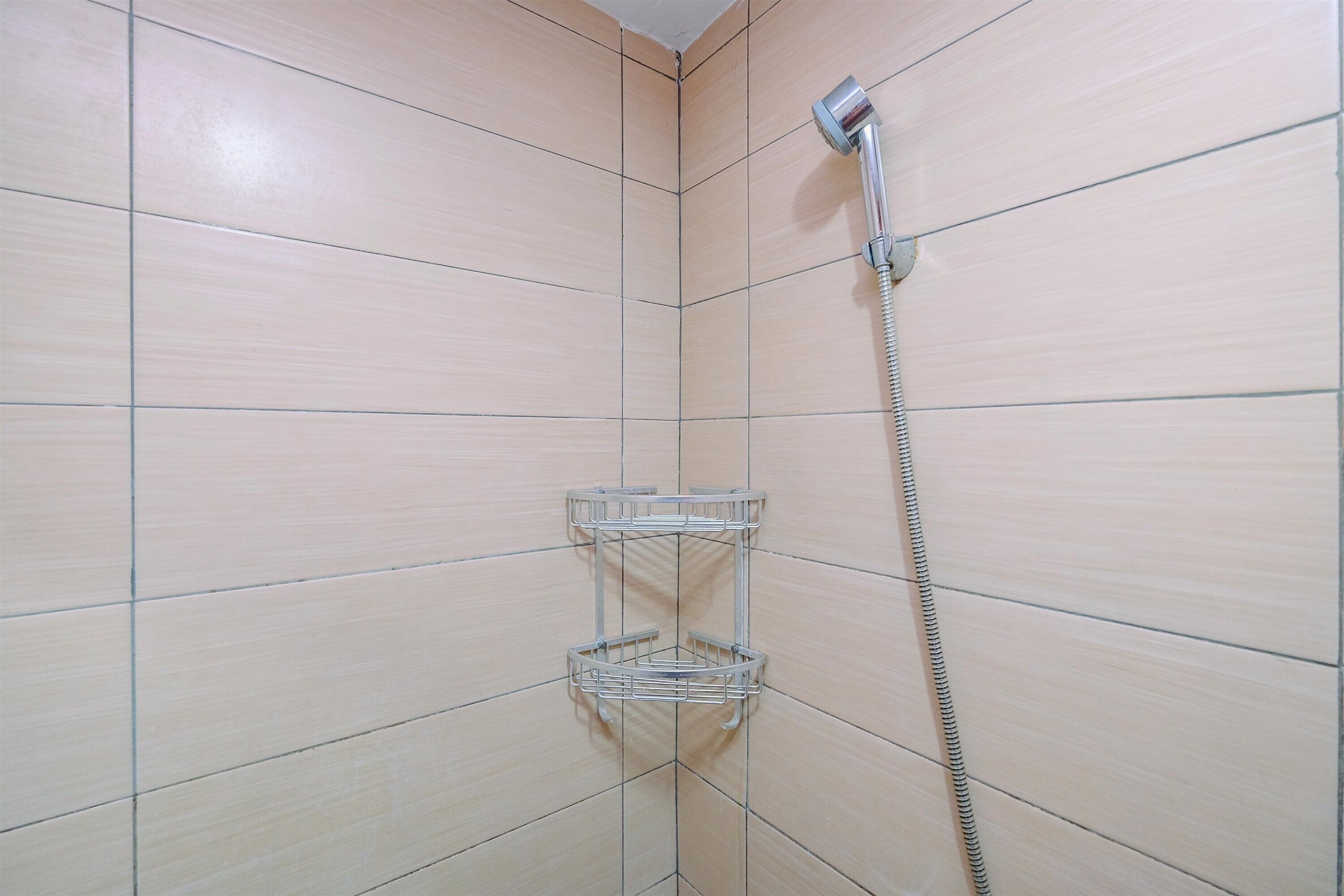 Ein Badezimmer im Eckbereich mit beigen Fliesen, einer Duschbrause und zwei Metallregalen.