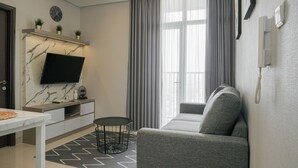 Een moderne woonkamer met een bank, een televisie bevestigd aan een marmeren muur, een klein tafeltje met pizza en een raam met gordijnen.