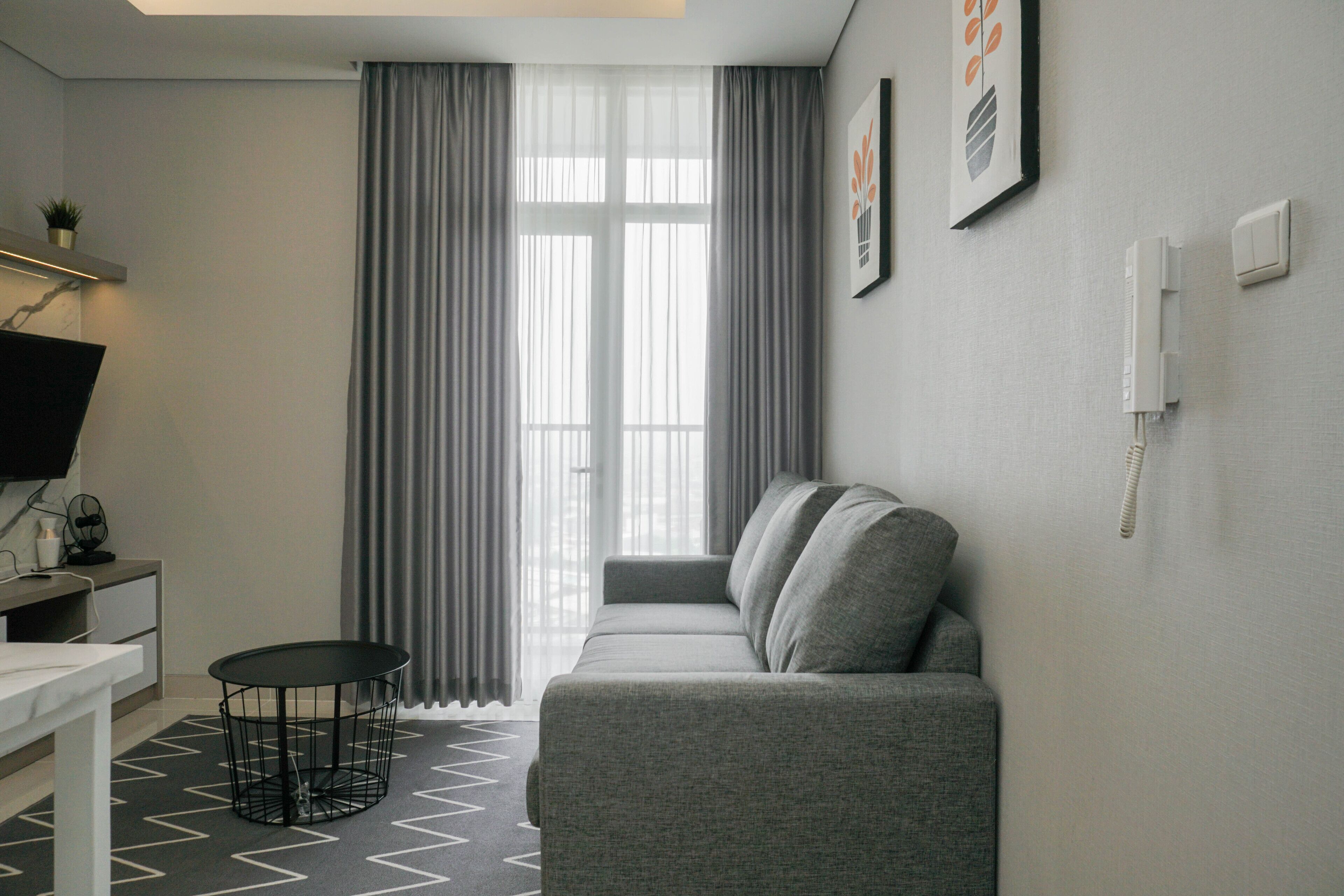 A modern living room with a grey sofa, a small round table, and a TV on a white stand.