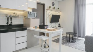 Een moderne keuken met witte kasten, een zwart aanrechtblad en een marmeren spatwand. Er is een magnetron, een koffiezetapparaat en een klein rond tafeltje met een stoel.