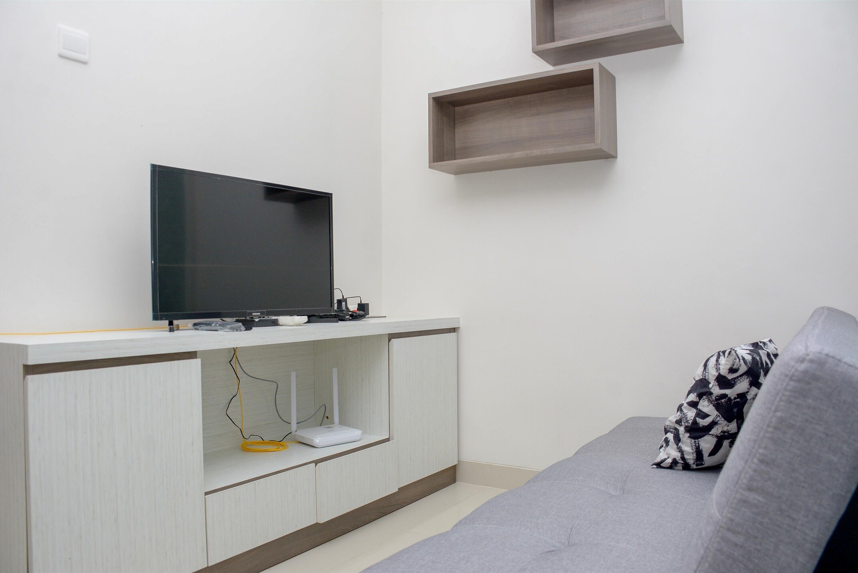 Una sala de estar moderna con un televisor de pantalla plana sobre una consola blanca, un sofá gris con un cojín estampado y estanterías empotradas.
