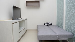 Ein kleiner Raum mit einem grauen Sofa, einem Fernseher auf einer Holzkommode und zwei Wandregalen.