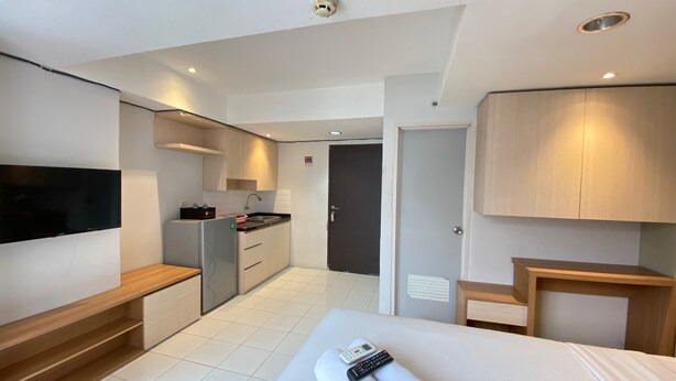 A modern hotel room with a bed, a TV, a small kitchenette, and a bathroom. - Spacious Studio Apartment At Jarrdin Cihampelas (Bandung)