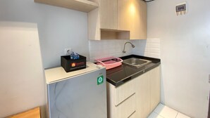 A compact kitchen with a built-in refrigerator, a sink, and wooden cabinets. - Spacious Studio Apartment At Jarrdin Cihampelas (Bandung)