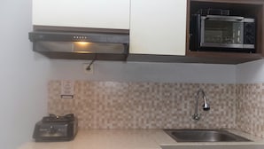 A kitchen with a microwave, a gas stove, a sink, and a tiled backsplash. - Homey And Comfort Studio At The Enviro Apartment (Cikarang)