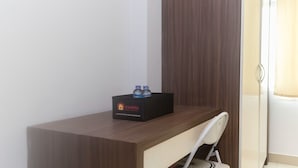 A wooden desk with a black box labeled 'travelio' containing two bottles, a white chair, and a window with curtains. - Homey And Comfort Studio At The Enviro Apartment (Cikarang)