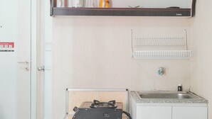 A kitchen with a gas stove, a sink, and a shelf above the stove holding a kettle, a coffee maker, and a canister. - Comfy Studio Green Pramuka City Apartment Near Mall (Jakarta)