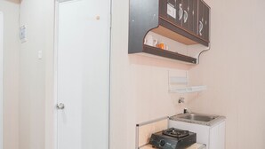 A compact kitchen with a gas stove, a sink, and a small cabinet above the counter. - Comfy Studio Green Pramuka City Apartment Near Mall (Jakarta)