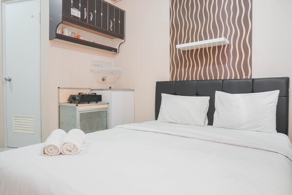 A hotel room with a bed, two pillows, a wardrobe, a desk with a computer, and a towel on the bed.