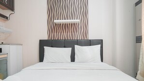 A neatly made bed with white bedding and pillows, a headboard, and a wall with a wavy pattern. - Comfy Studio Green Pramuka City Apartment Near Mall (Jakarta)