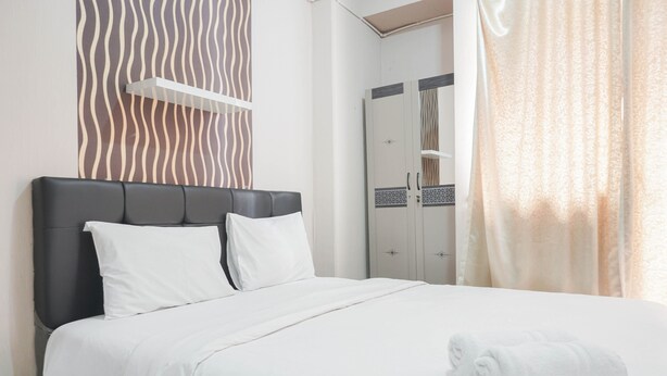 A neatly made bed with white linens and pillows, a black headboard, and a rolled white towel on the bed. - Comfy Studio Green Pramuka City Apartment Near Mall (Jakarta)