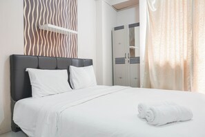 A neatly made bed with white linens and pillows, a black headboard, and a rolled white towel on the bed.