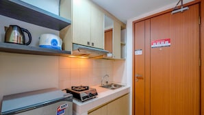 A compact kitchen with a refrigerator, a kettle, a coffee maker, and a stove. - Homey And Simply Studio Room At Margonda Residence 3 Apartment (Depok)