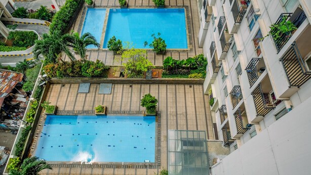 A rooftop swimming pool with two separate sections, surrounded by lush greenery and residential buildings. - Homey And Simply Studio Room At Margonda Residence 3 Apartment (Depok)