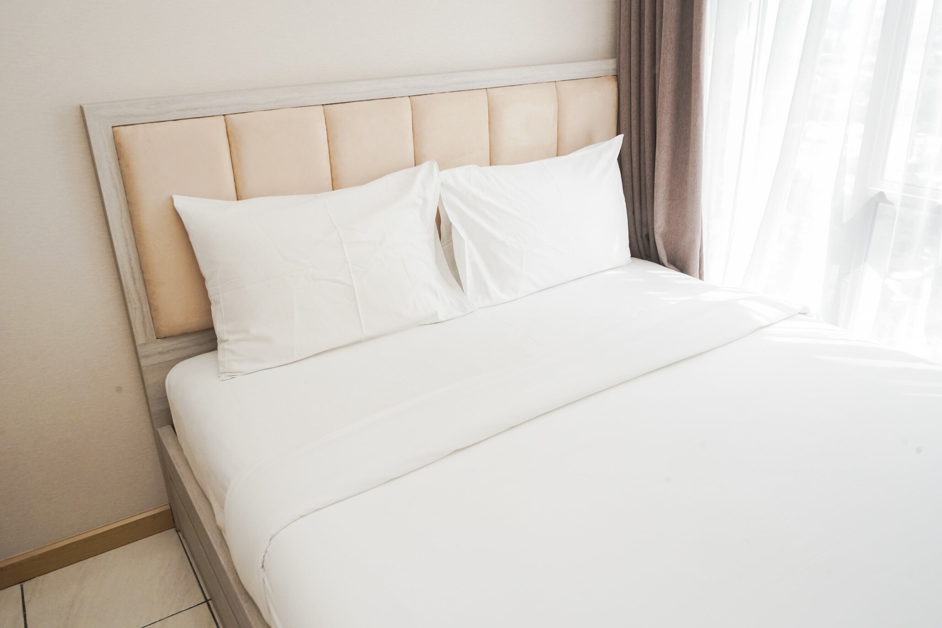 A neatly made bed with white linens and a light-colored headboard.
