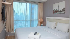 A hotel room with a large bed, a television mounted on the wall, a window with curtains, a lamp, and a painting of a cityscape.