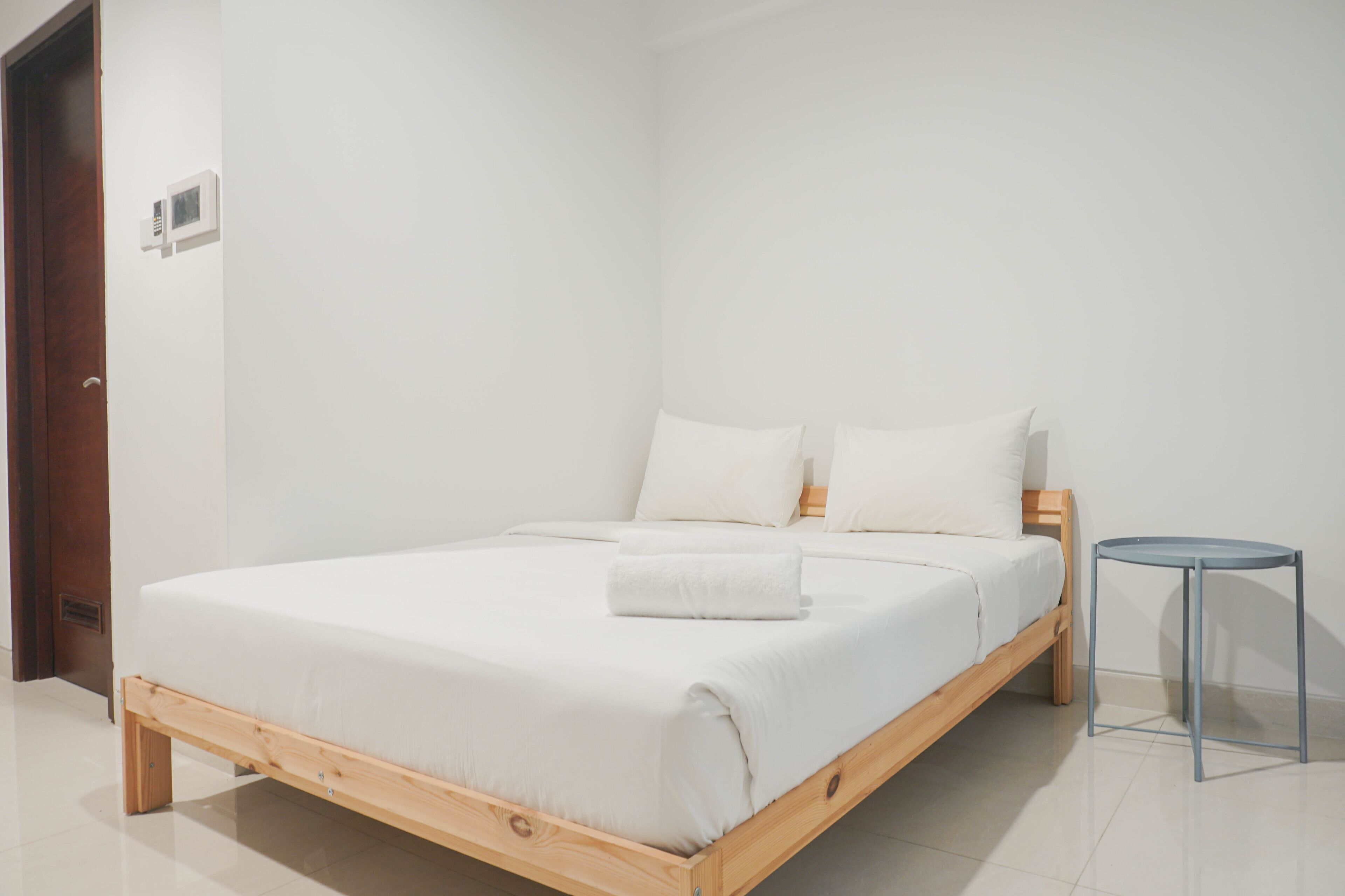 A minimalist bedroom with a wooden bed, white bedding, and a small side table.