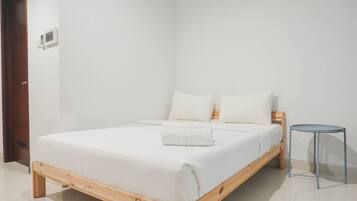A minimalist bedroom with a wooden bed, white bedding, and a small side table.