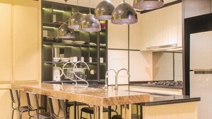 A modern kitchen with a central island, bar stools, pendant lighting, and stainless steel appliances. - Comfort And Spacious 3Br At Branz Bsd City Apartment (Pagedangan)