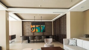 A modern living room with a sofa, coffee table, and chairs. There is a dining area with a table and chairs. The room has a large abstract painting on the wall. - Comfort And Spacious 3Br At Branz Bsd City Apartment (Pagedangan)