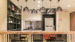 A kitchen with a marble countertop, four bar stools, and pendant lighting. - Comfort And Spacious 3Br At Branz Bsd City Apartment (Pagedangan)