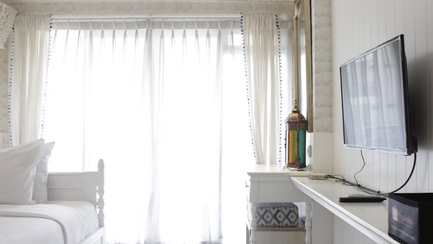 A bedroom with a white bed, a television on a white dresser, and a window with sheer curtains. - Elegant & Stylish Studio At Gateway Pasteur Apartment (Cimahi)