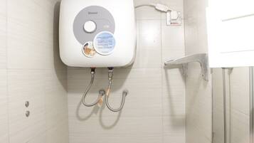 A bathroom with a white tiled wall, a white toilet with a control panel, and two metal pipes.