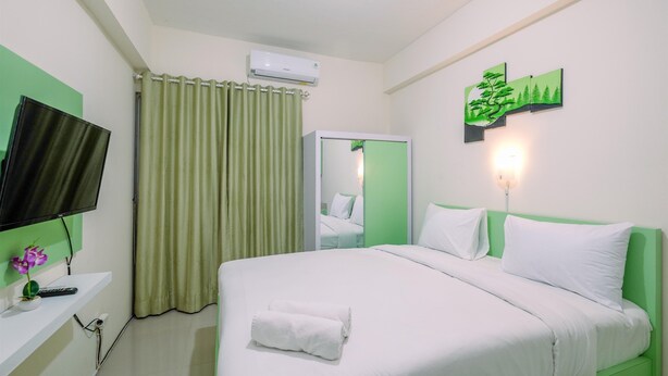 Quarto de hotel com uma cama, televisão, espelho, parede verde e uma pintura.
