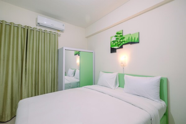 A hotel room with a bed, green curtains, a wall-mounted air conditioner, and a green wall decoration.