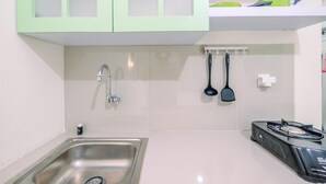 Uma cozinha compacta com pia de aço inoxidável, fogão a gás e armários verde-claros.