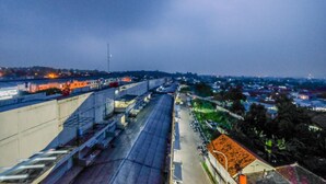 Vista aérea de um horizonte urbano ao entardecer, com uma ponte em destaque, edifícios e uma colina distante.